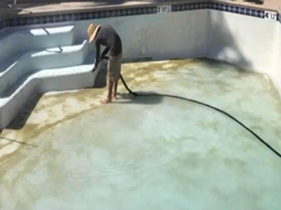 Drained plaster pool with stained floor and a hose laid across it